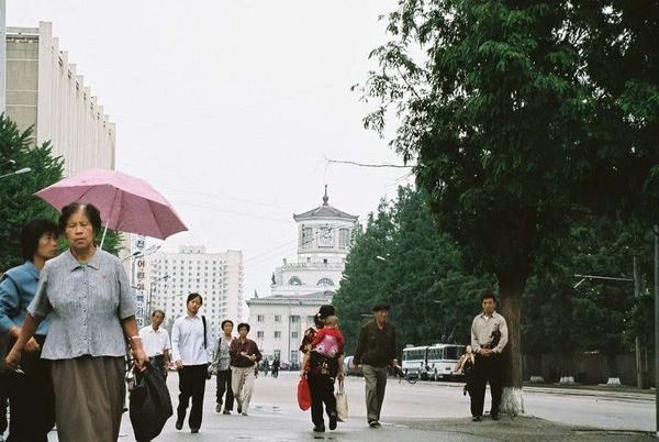 朝鮮民主主義人民共和国・DMZ「2005年金正日政権下の北朝鮮」の写真：人民。平城鉄道駅を背景に
人民と言葉を交...